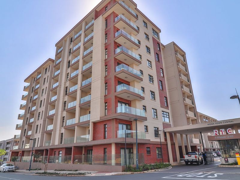 Exterior view of the Ridge Town Central apartment complex, featuring modern brick architecture, glass balconies, and a secure gated entrance.