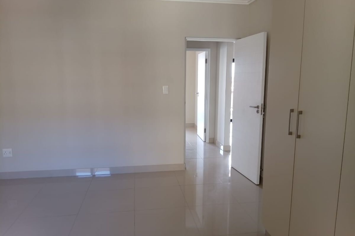 A bright, empty bedroom featuring neutral tiled flooring, built-in cupboards, and clean finishes, offering a versatile space ready for personalization.