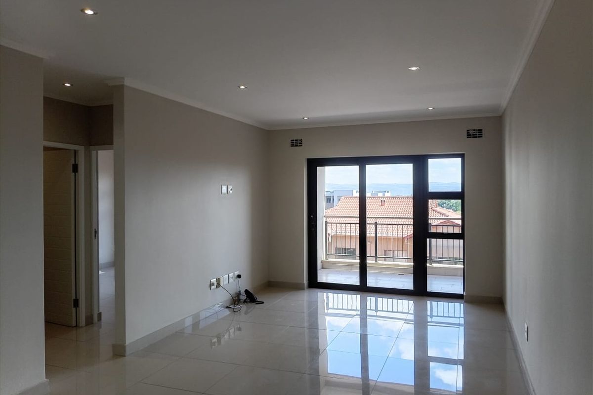 Spacious, empty living area featuring neutral tiled floors, recessed downlighting, and large sliding glass doors providing access to a private balcony.