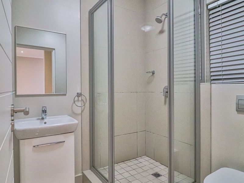A clean, modern bathroom featuring a glass-enclosed shower, vanity basin with storage, wall-mounted mirror, and a concealed cistern toilet.