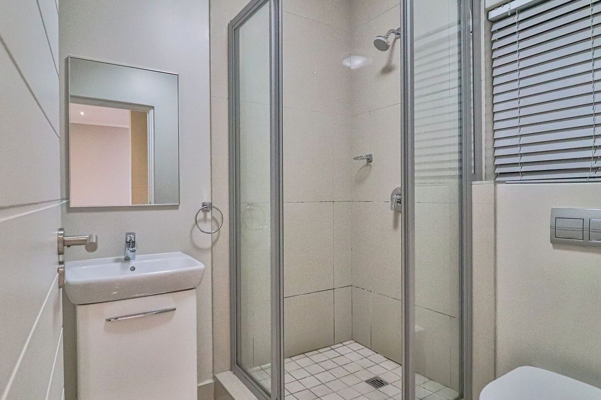A clean, modern bathroom featuring a glass-enclosed shower, vanity basin with storage, wall-mounted mirror, and a concealed cistern toilet.