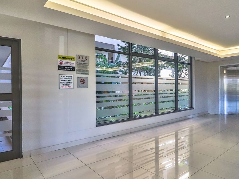 A clean and modern apartment building entrance lobby featuring polished floor tiles, recessed ceiling lighting, and a functional elevator access point.