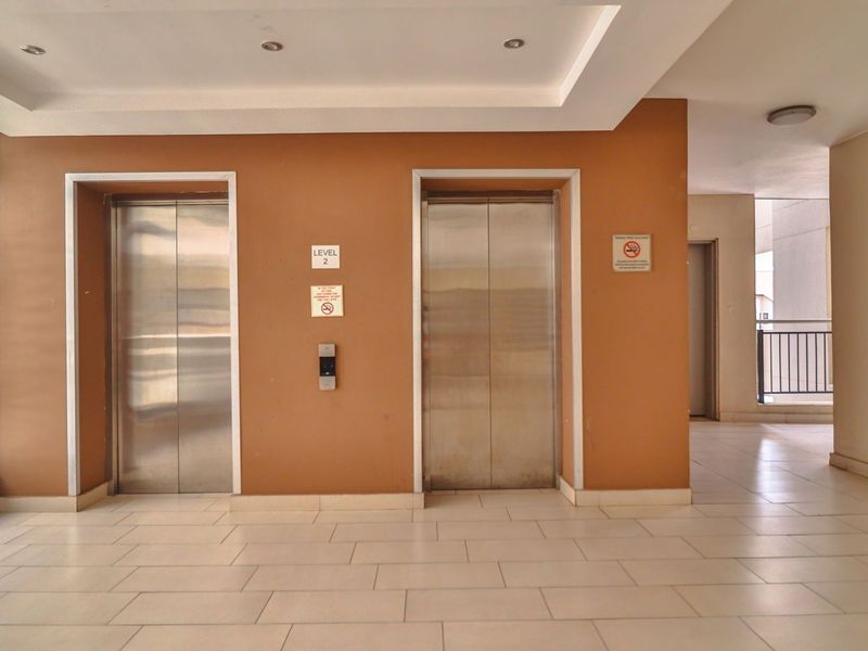 A clean and well-maintained apartment building elevator lobby featuring stainless steel lift doors, tiled flooring, and recessed ceiling lighting.