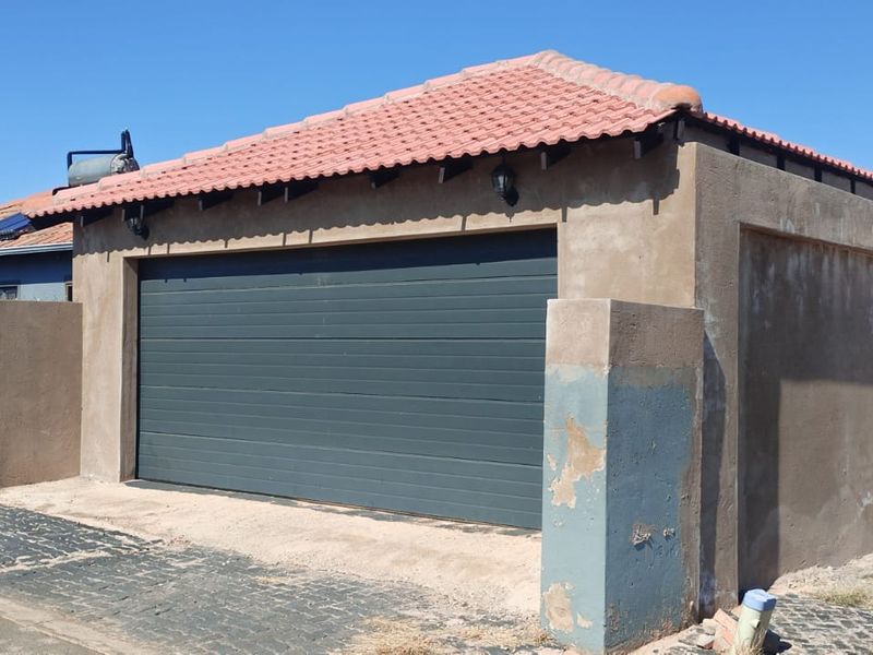 A detached garage structure featuring a sectional door, tiled roof, and solar geyser, with visible exterior wall paint deterioration.