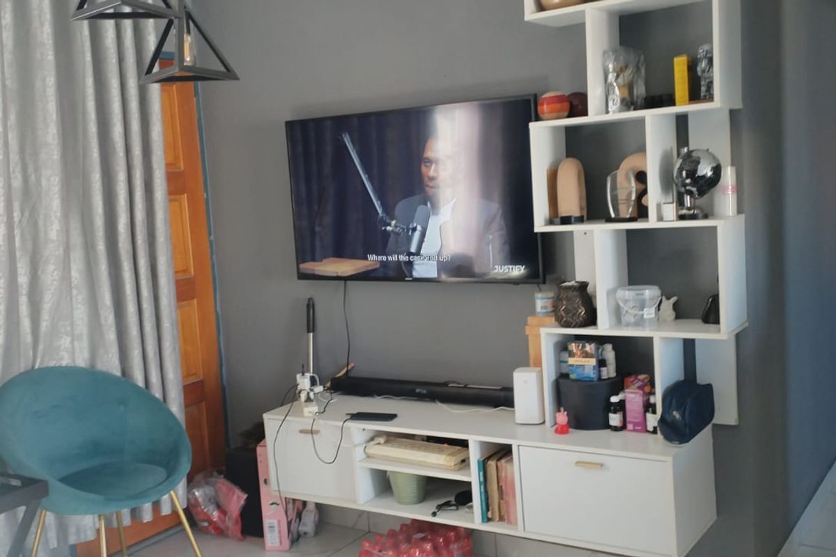 A living room area featuring a wall-mounted television, a built-in shelving unit, and tiled flooring.
