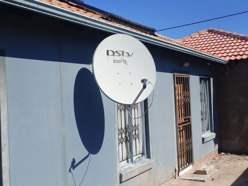 Rear exterior view of the property featuring a satellite dish, security gates on windows and doors, and a tiled roof.