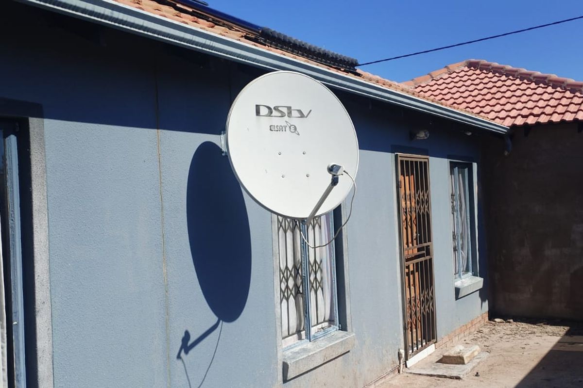 Rear exterior view of the property featuring a satellite dish, security gates on windows and doors, and a tiled roof.