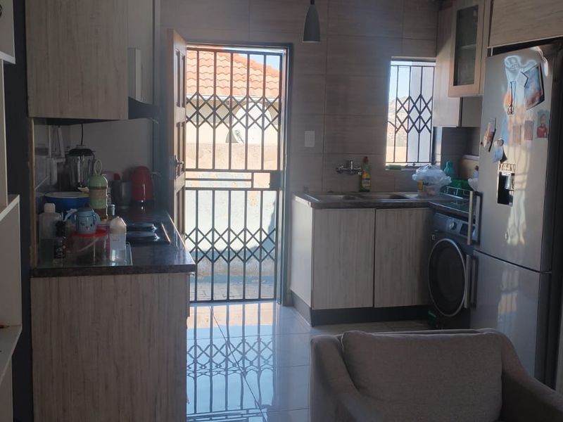 A functional kitchen featuring built-in cabinetry, laminate countertops, tiled flooring, and direct access to the exterior via a security gate.