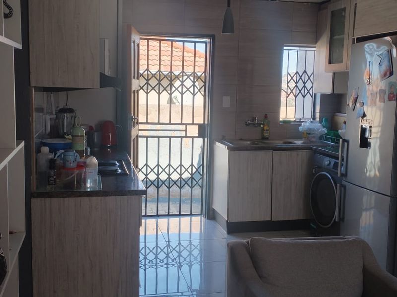 Compact kitchen featuring light wood-finish cabinetry, laminate countertops, tiled flooring, and direct access to the exterior via a security gate.
