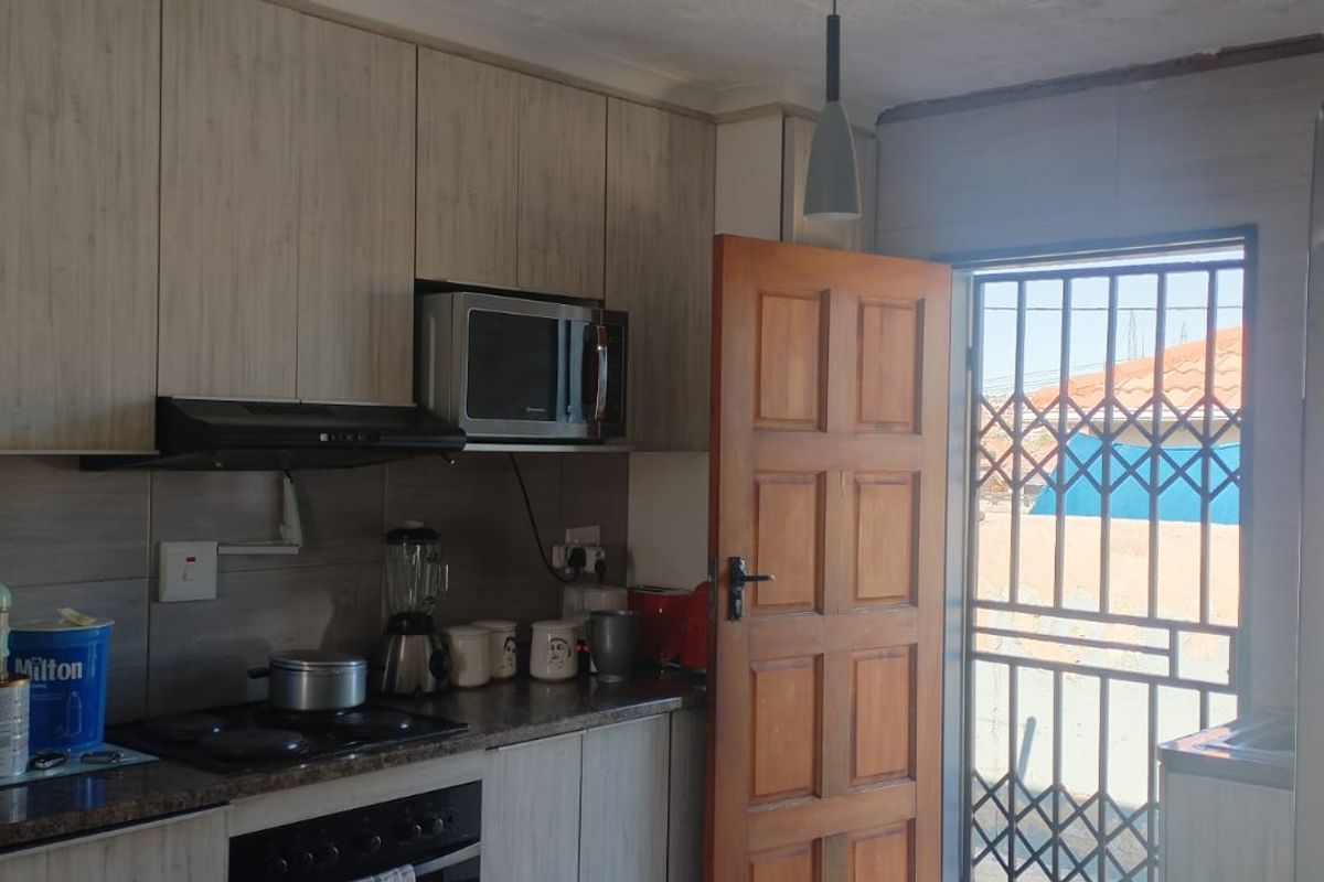 A functional kitchen featuring wood-look cabinetry, built-in oven and hob, extractor fan, and direct access to the exterior via a secure door.
