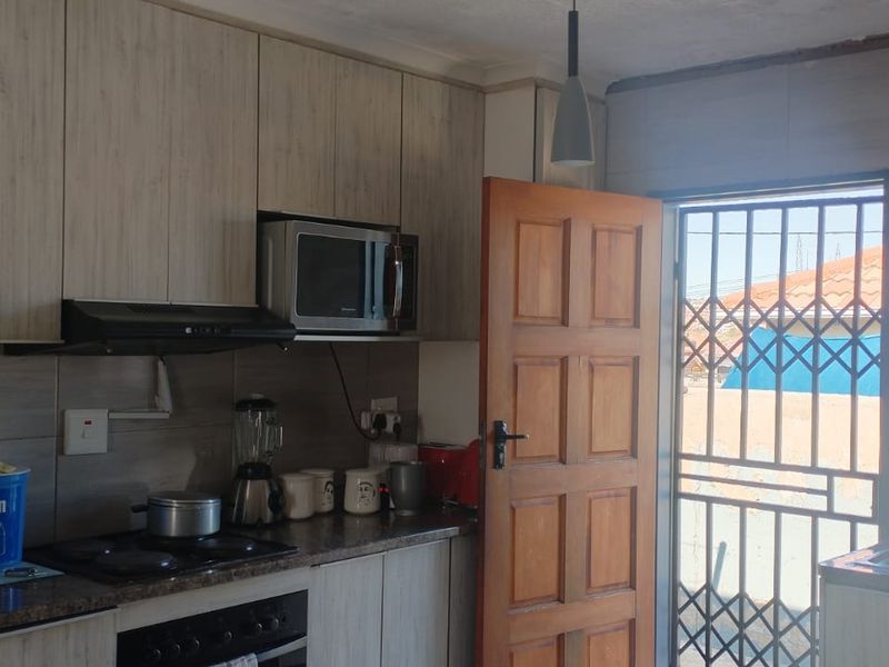 A functional kitchen featuring wood-look cabinetry, built-in oven and hob, extractor fan, and direct access to the exterior via a secure door.