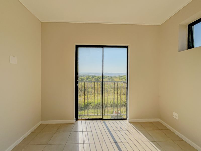 An empty bedroom featuring neutral tiled flooring, a sliding glass door leading to a balcony, and scenic natural views.