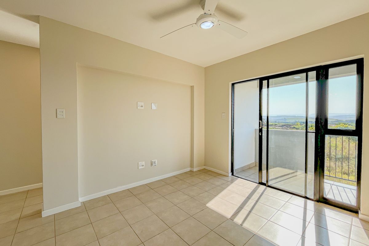 A bright, empty living room featuring tiled floors, a ceiling fan, and large sliding glass doors that open onto a balcony with scenic views.