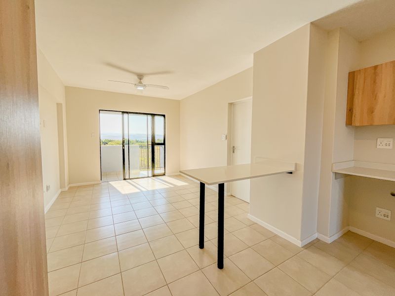 Bright open-plan living area featuring tiled floors, a ceiling fan, and a built-in breakfast bar, with direct access to a balcony.