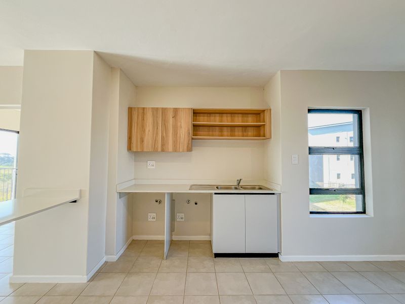 A clean, modern kitchen area featuring built-in cabinetry, a stainless steel sink, and tiled flooring, ready for appliance installation.