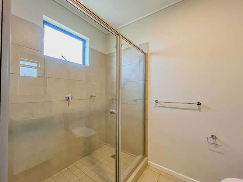 A clean, functional bathroom featuring a glass-enclosed shower with tiled walls, chrome fixtures, and a top-hung window for natural light.
