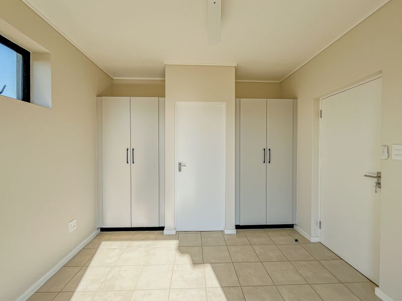 A clean, empty bedroom featuring neutral tiled flooring, built-in cupboards, and a ceiling fan, offering a bright and versatile living space.