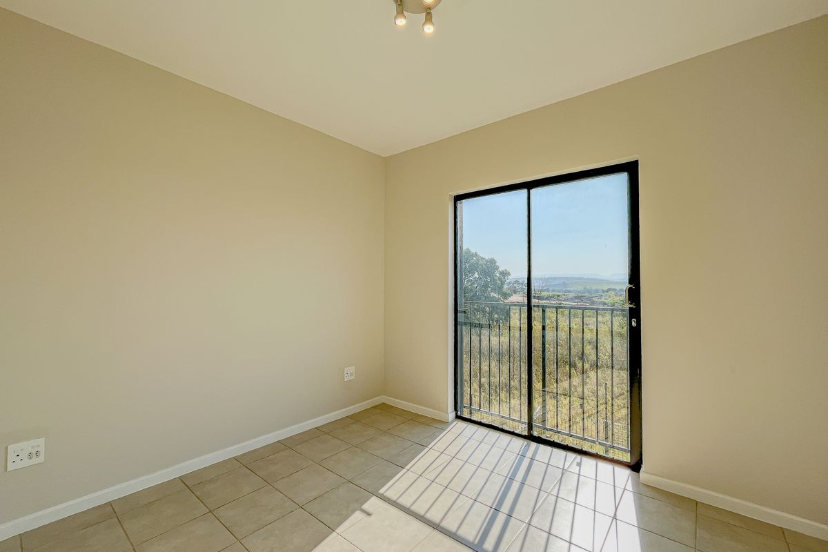 A bright, empty bedroom featuring neutral tiled flooring and a sliding glass door that opens to a balcony with scenic views.
