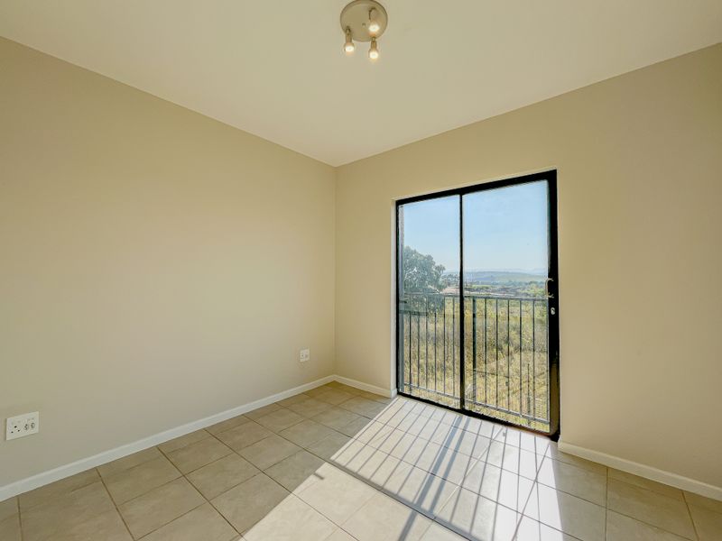 A bright, empty bedroom featuring neutral tiled flooring and a sliding glass door that opens to a balcony with scenic views.