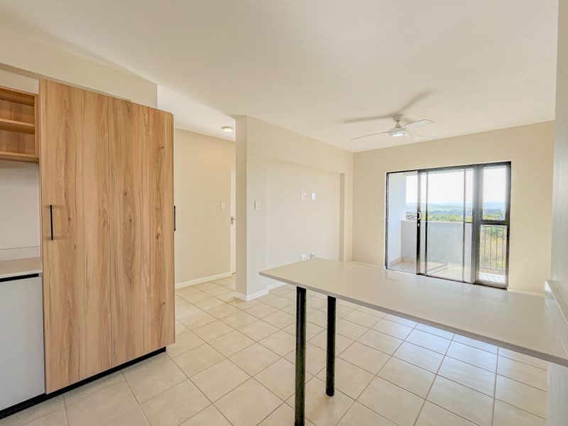 Bright open-plan living area featuring tiled floors, a built-in breakfast bar, ceiling fan, and sliding door access to a balcony with scenic views.