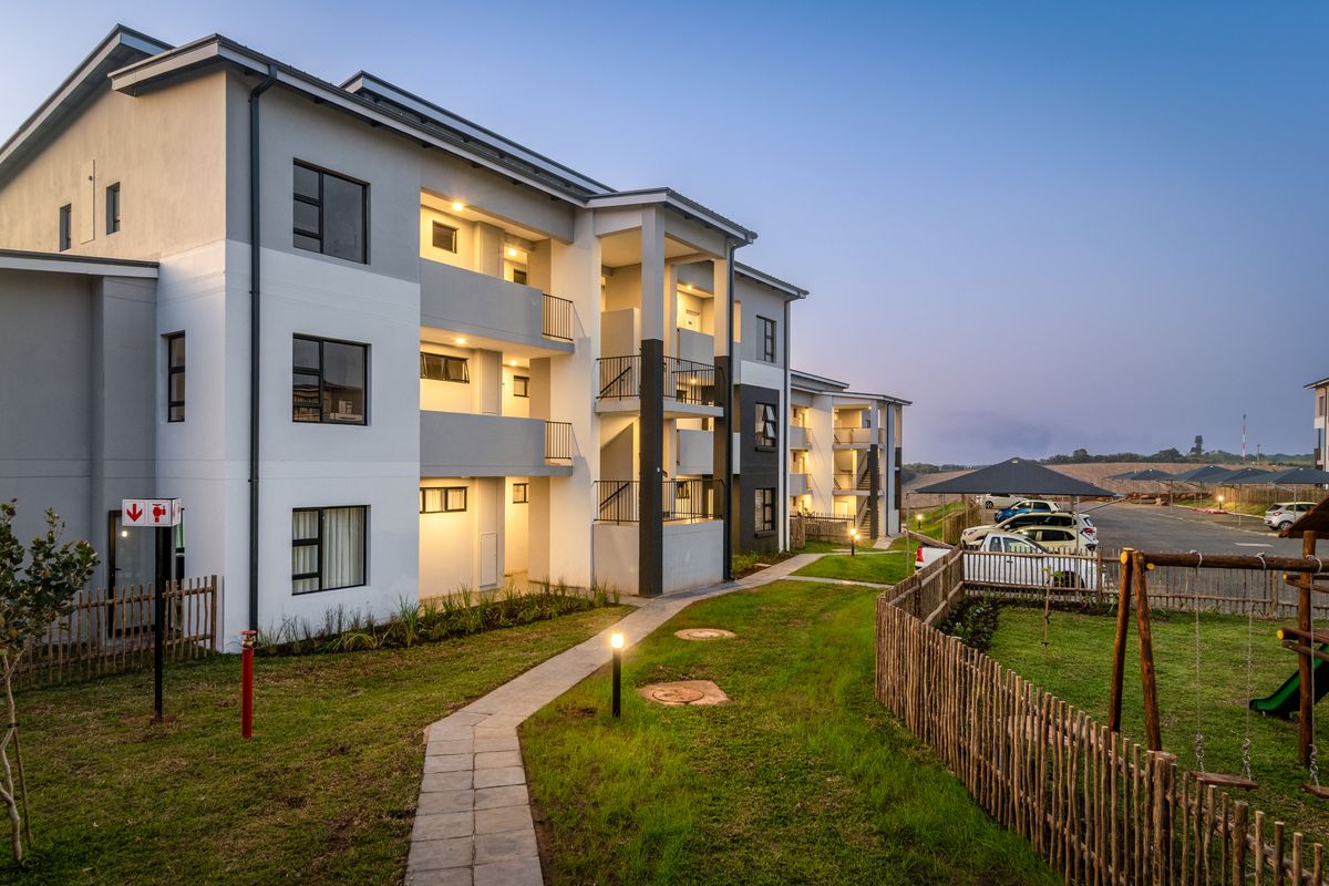 Modern apartment complex exterior featuring paved walkways, landscaped garden areas, private balconies, and covered parking facilities.