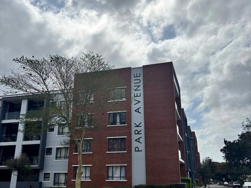 Exterior view of the Park Avenue apartment complex featuring a modern brick facade, balconies, and surrounding landscaped grounds.