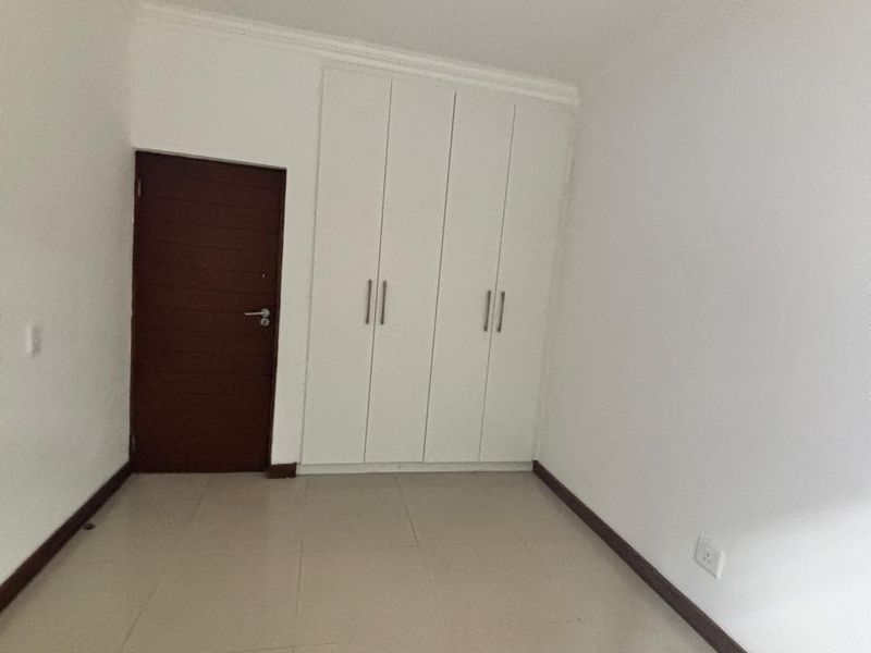 An empty bedroom featuring neutral tiled flooring, built-in white cupboards, and a dark wood door.