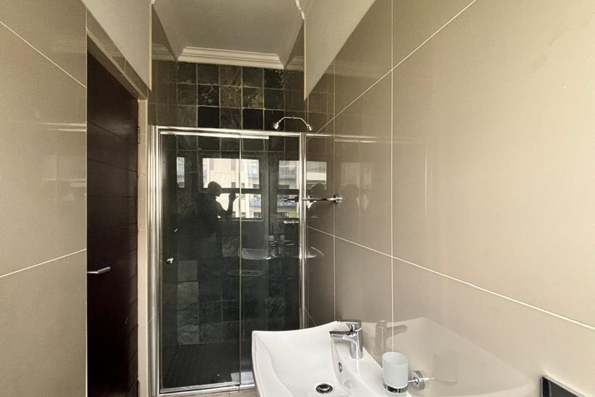 A compact bathroom featuring a wall-mounted basin, chrome fixtures, and a glass-enclosed shower with tiled finishes throughout.