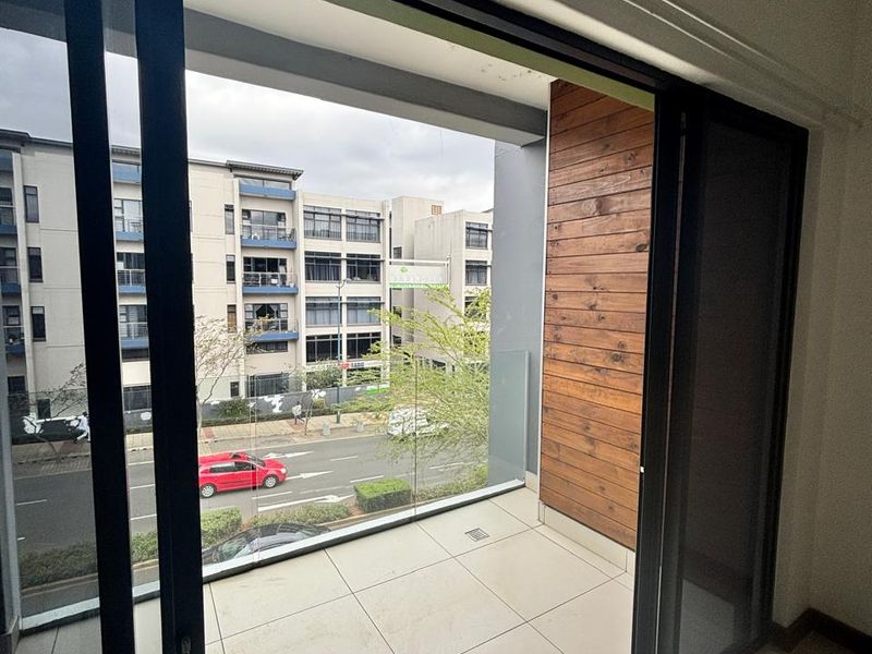 A modern apartment balcony featuring tiled flooring, a glass balustrade, and decorative timber wall cladding, offering an urban street view.