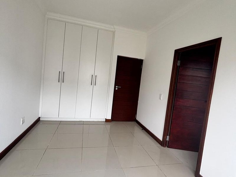 A clean, empty bedroom featuring neutral tiled flooring, built-in white cupboards, and dark wood internal doors.