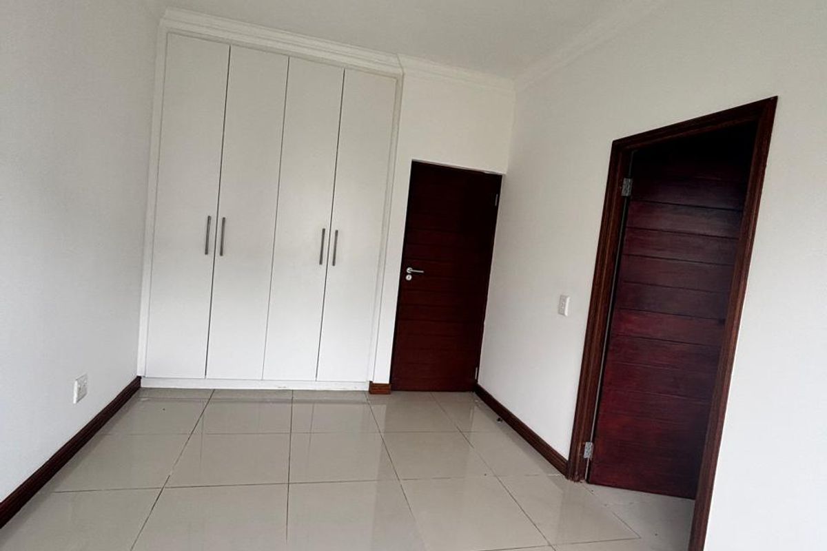 A clean, empty bedroom featuring neutral tiled flooring, built-in white cupboards, and dark wood internal doors.