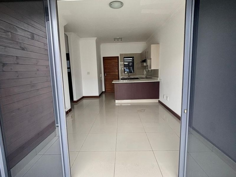 An open-plan living and kitchen area featuring neutral tiled flooring, modern cabinetry, and large sliding glass doors leading to an outdoor space.