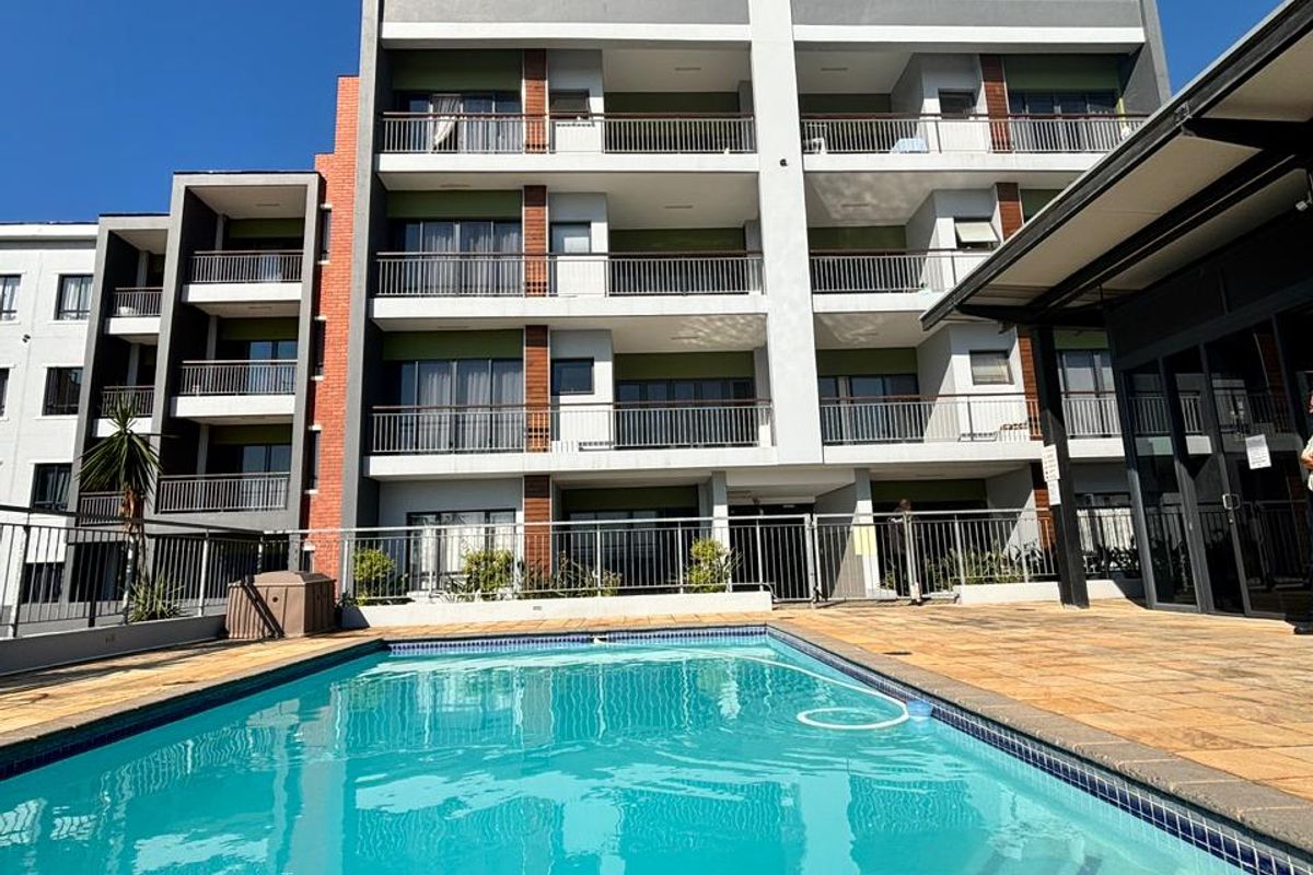 A well-maintained apartment complex featuring a clear swimming pool, paved deck area, and multi-story residential units with private balconies.