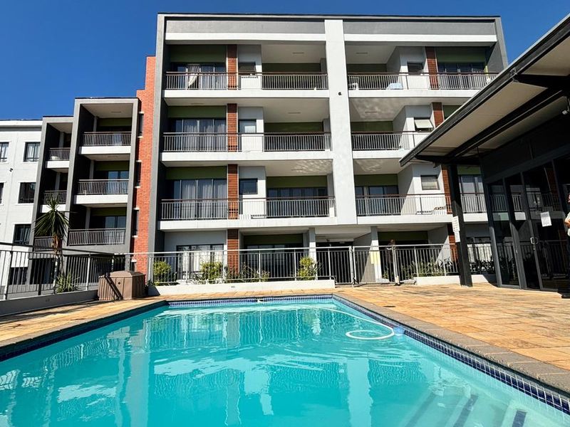 A well-maintained apartment complex featuring a clear swimming pool, paved deck area, and multi-story residential units with private balconies.