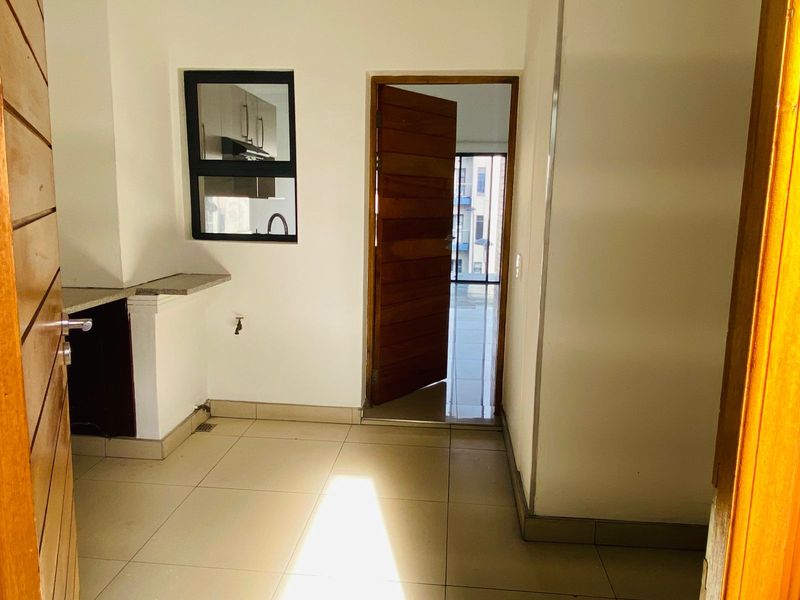 A compact, empty kitchen area featuring tiled flooring, a stone countertop, and a wooden door leading to an adjacent living space.