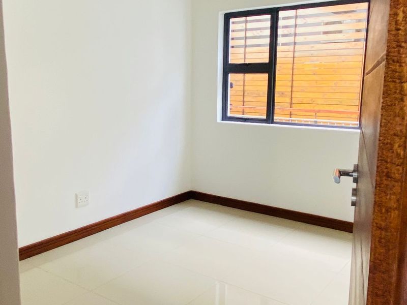 A clean, empty bedroom featuring neutral tiled flooring, white walls, and an aluminium-framed window with a curtain rod.