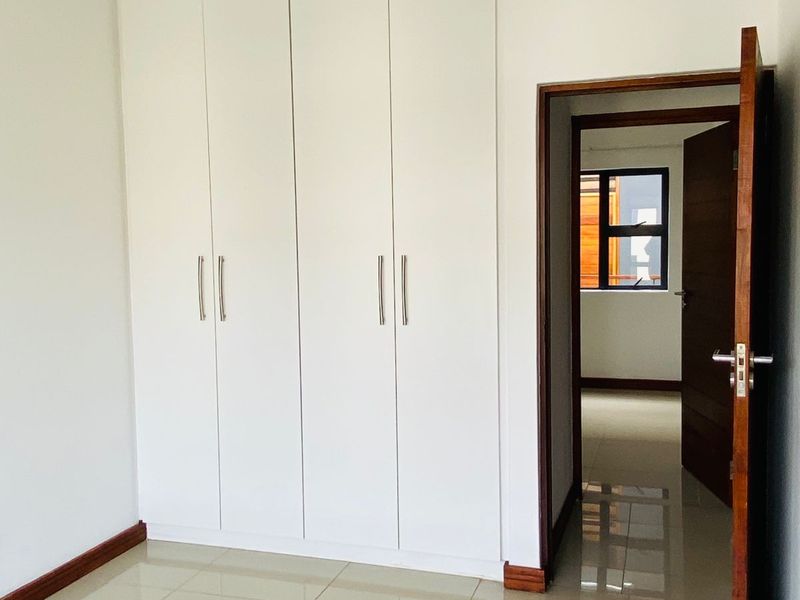 A clean, empty bedroom featuring modern white built-in cupboards, neutral tiled flooring, and a wooden door frame leading to an adjacent room.