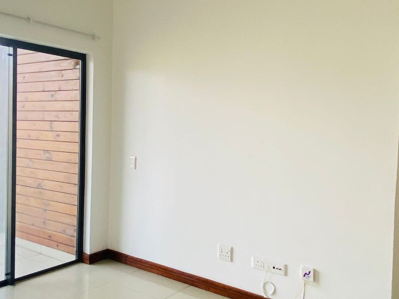 An empty living area featuring neutral tiled flooring, timber skirting boards, and a sliding glass door providing access to an outdoor space.