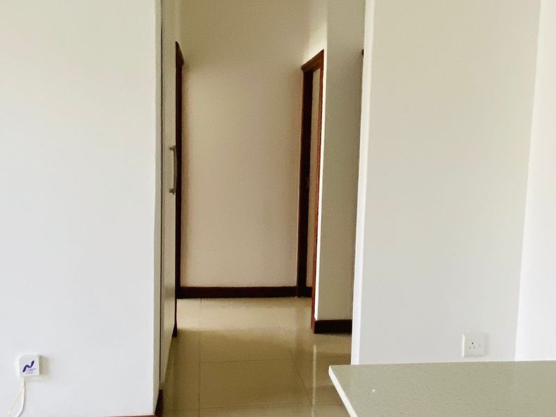 A clean, empty hallway featuring neutral tiled flooring, white walls, and wooden door frames, providing access to adjacent rooms.