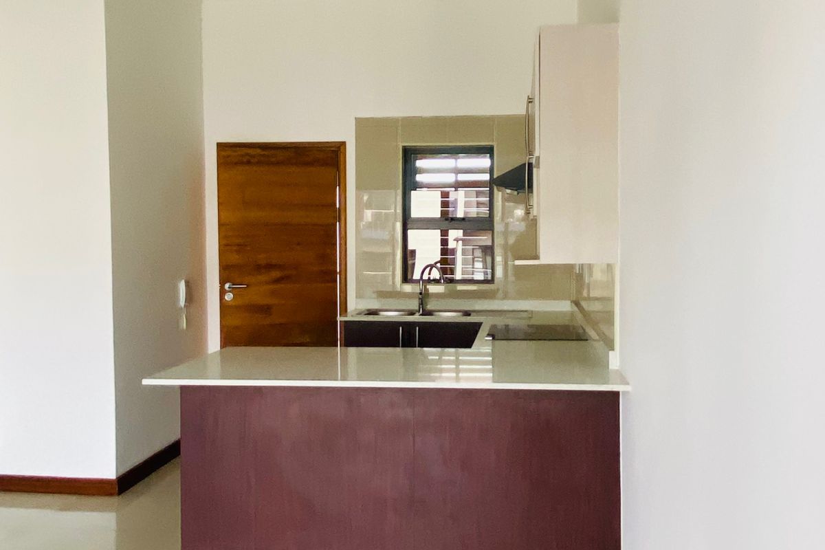 A clean, modern kitchen featuring dark wood cabinetry, stone countertops, a double sink, and a tiled backsplash, integrated into an open-plan living space.