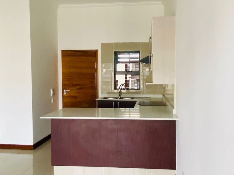 A clean, modern kitchen featuring dark wood cabinetry, stone countertops, a double sink, and a tiled backsplash, integrated into an open-plan living space.