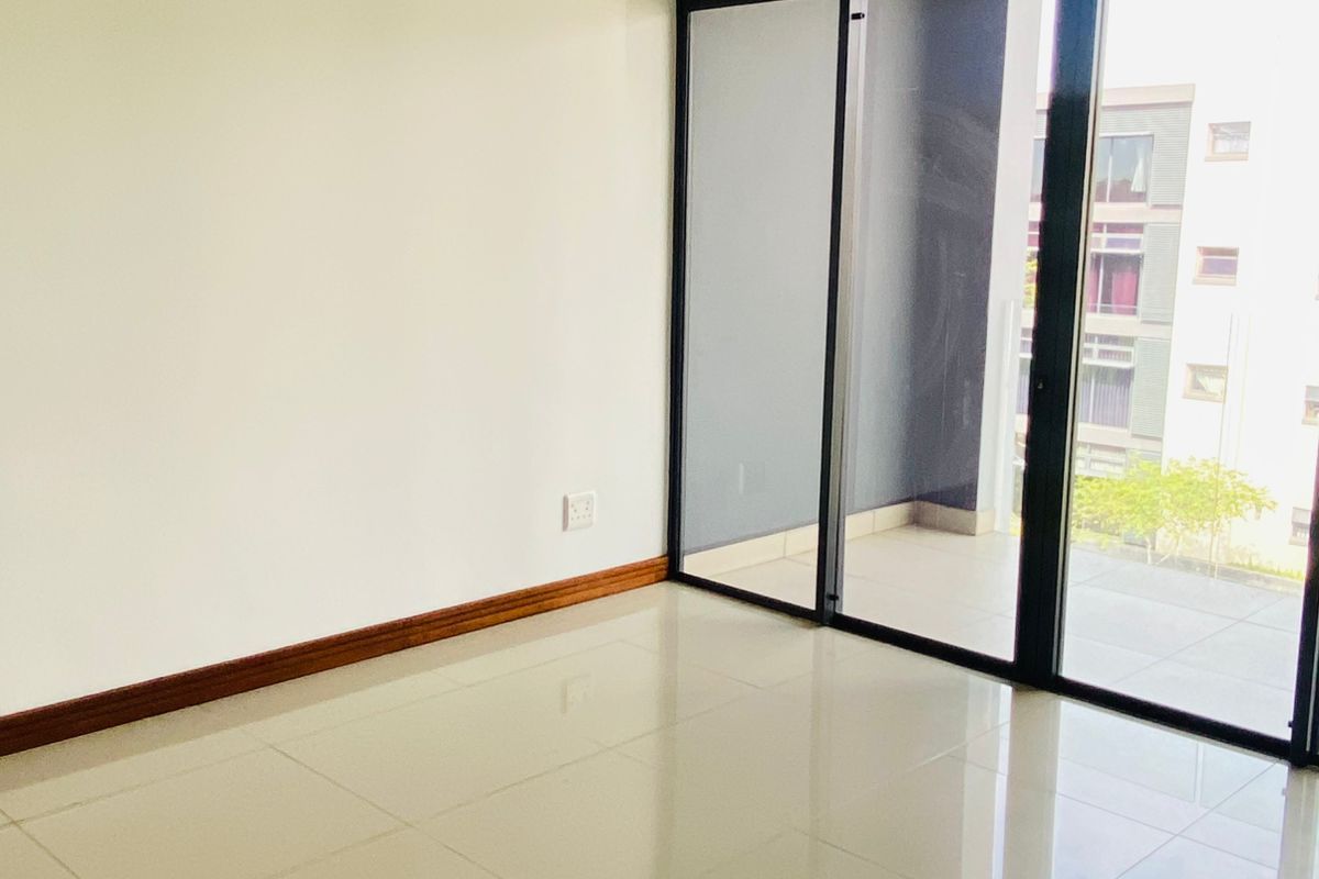 A bright, empty living area featuring polished tile flooring and large sliding glass doors that provide access to an outdoor balcony space.