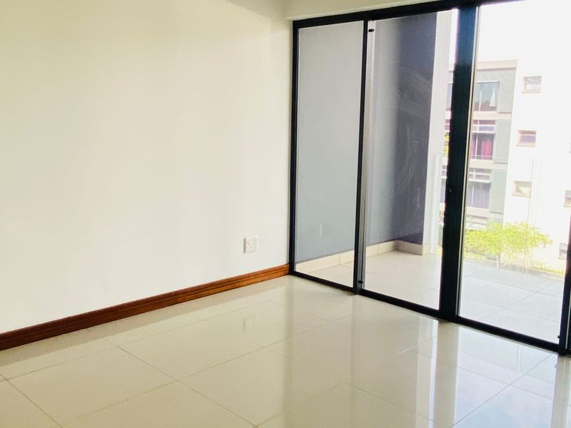 A bright, empty living area featuring polished tile flooring and large sliding glass doors that provide access to an outdoor balcony space.