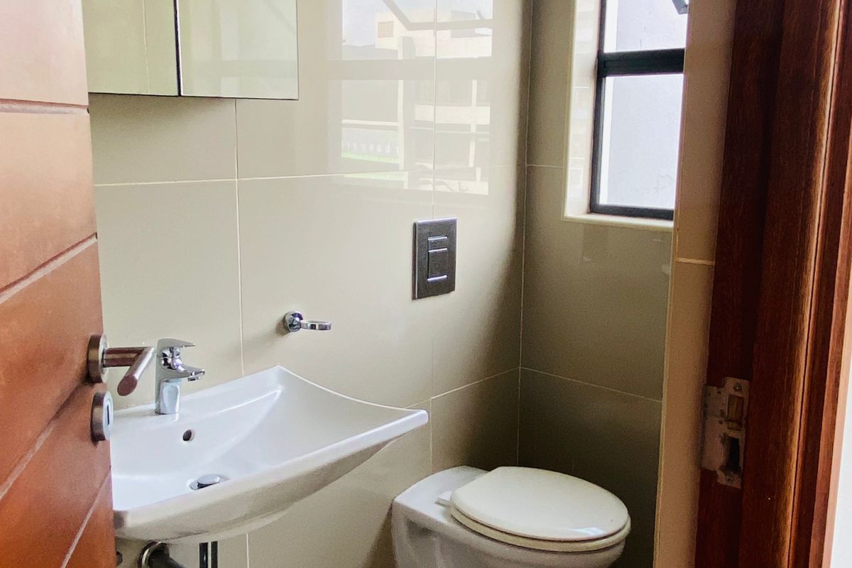 A modern, compact bathroom featuring a wall-hung basin, wall-mounted toilet, and a mirrored medicine cabinet with neutral wall and floor tiling.