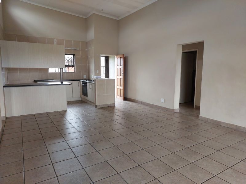 Spacious open-plan living area featuring tiled floors and a functional kitchen with built-in cabinetry, oven, and hob, offering a clean, blank canvas.