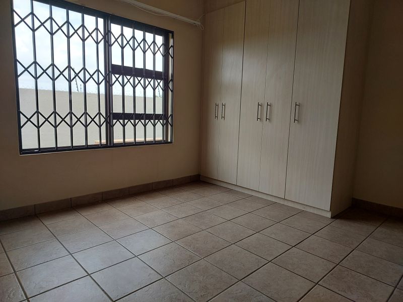 An empty bedroom featuring tiled flooring, built-in cupboards, and a window fitted with a security gate.