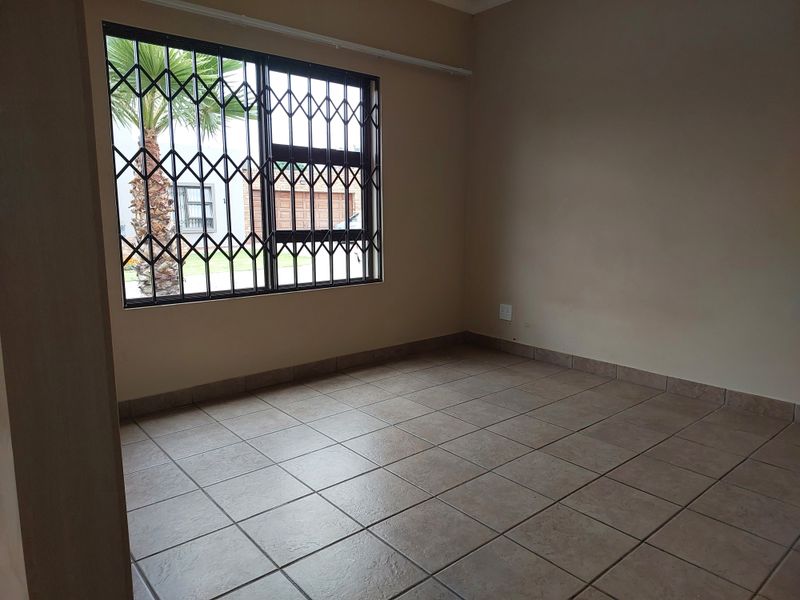 An empty bedroom featuring neutral tiled flooring and a window fitted with a security gate.