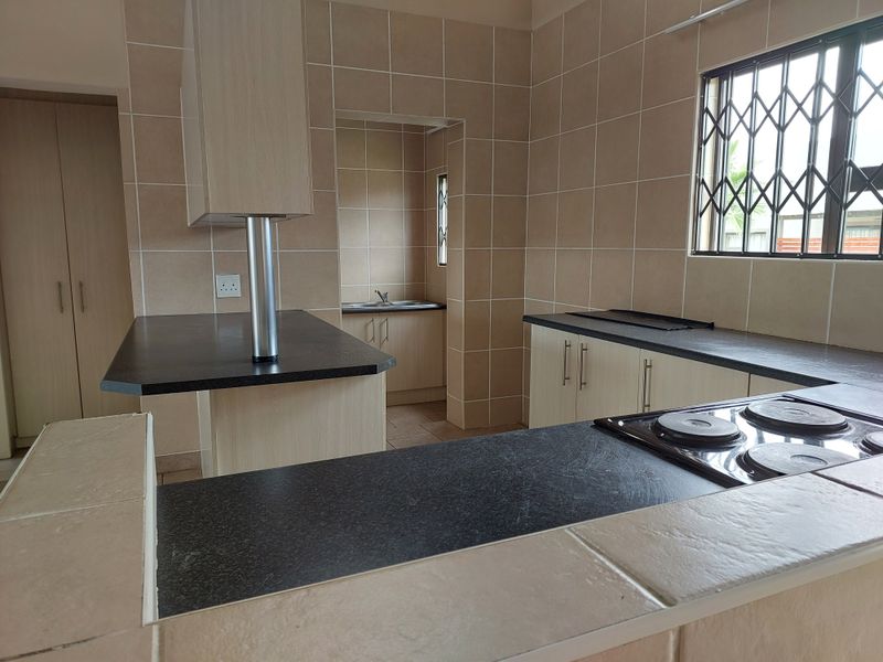 A functional kitchen featuring built-in cabinetry, laminate countertops, an electric hob, and a separate scullery area with a sink.