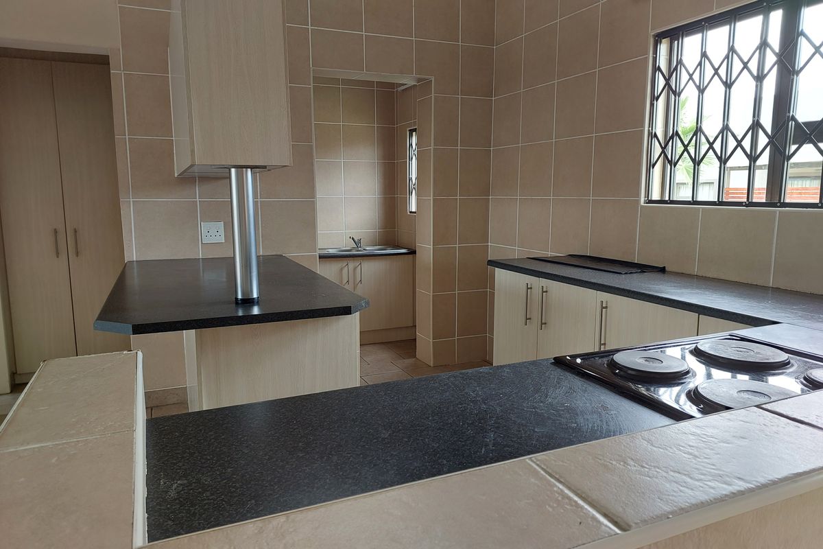 A functional kitchen featuring built-in cabinetry, laminate countertops, an electric hob, and a separate scullery area with a sink.