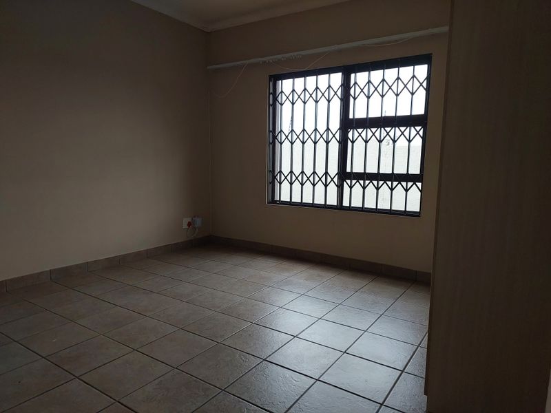 An empty bedroom featuring tiled flooring, a window with a security gate, and a built-in cupboard.